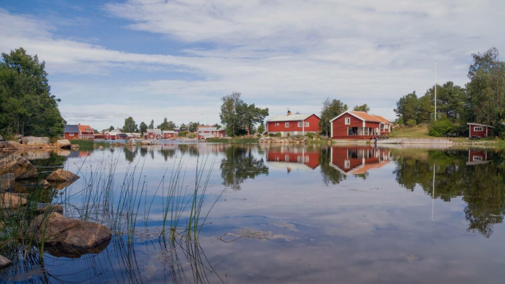 Maisons rouges traditionnelles au bord de l'eau à Hälsingland, créant une scène paisible et idyllique.