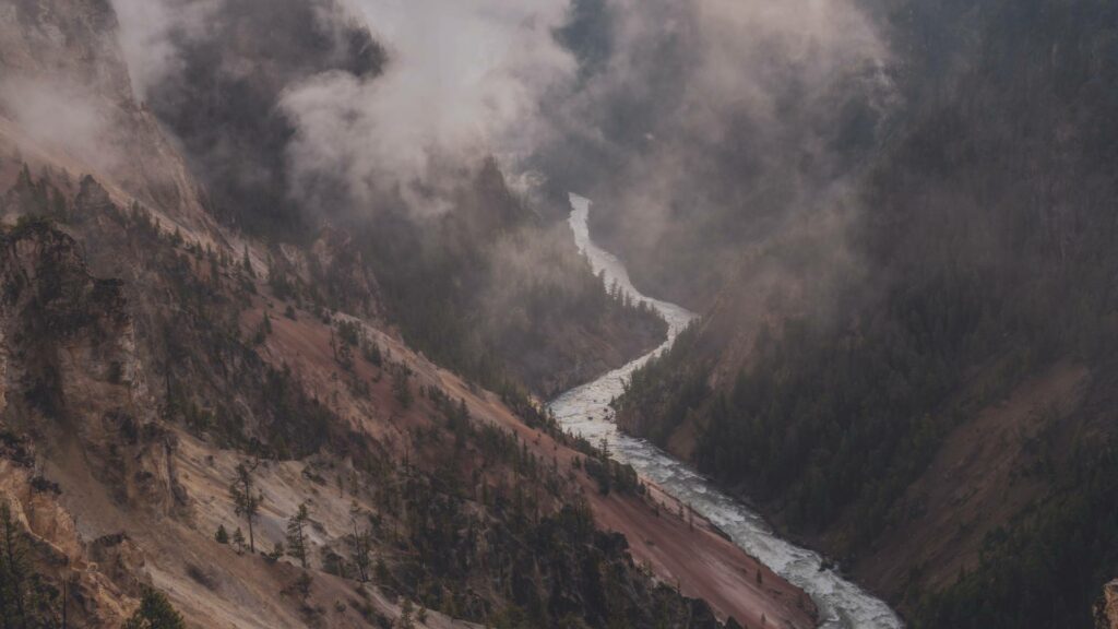 Rivière entourée de montagnes et enveloppée de brume à Yellowstone, créant une atmosphère mystique et paisible.