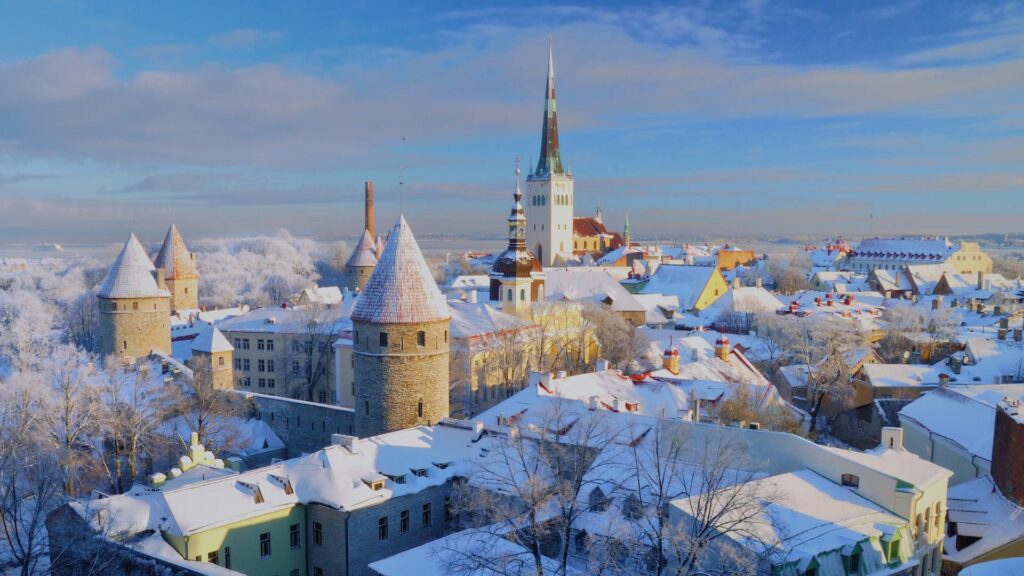 Vue hivernale de la vieille ville de Tallinn avec des toits enneigés et des rues pavées, entourée de remparts médiévaux.