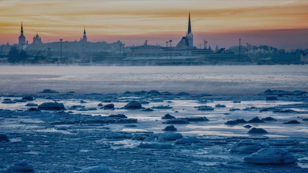 Coucher de soleil sur la mer Baltique vu depuis Tallinn, avec des reflets dorés dans l’eau et des paysages enneigés.