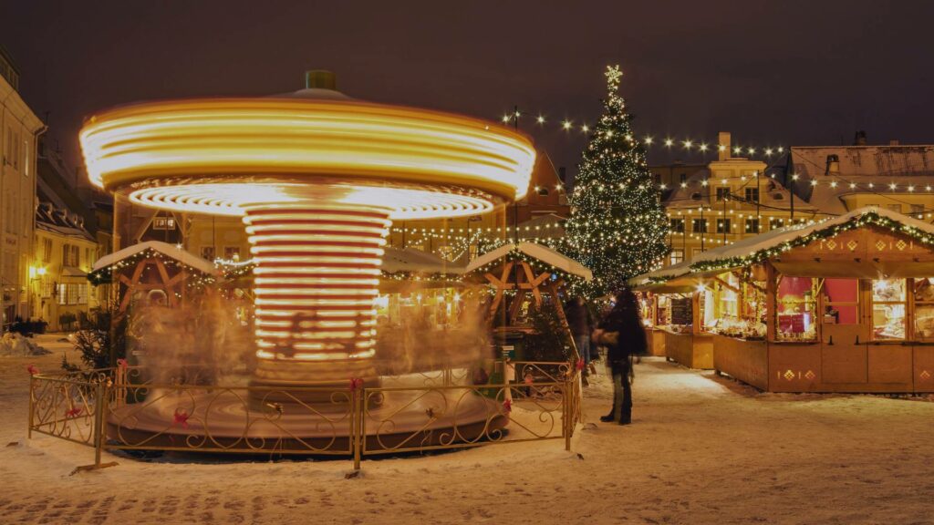 Marché de Noël de Tallinn sur la place de l’Hôtel de Ville, avec un grand sapin illuminé et des chalets en bois sous la neige.