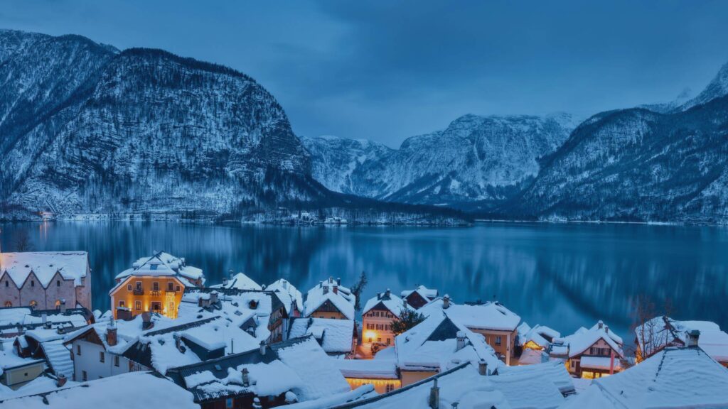 Village de Hallstatt illuminé le soir, avec des lumières qui se reflètent dans le lac enneigé.